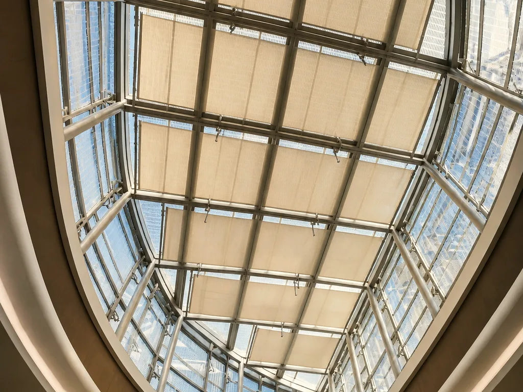 Light-filtering shade panels beneath a glass atrium roof