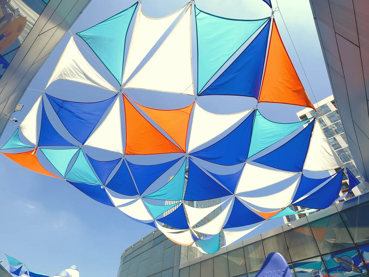 Blue, turquoise, white, and orange shade sails above an outdoor recreation area